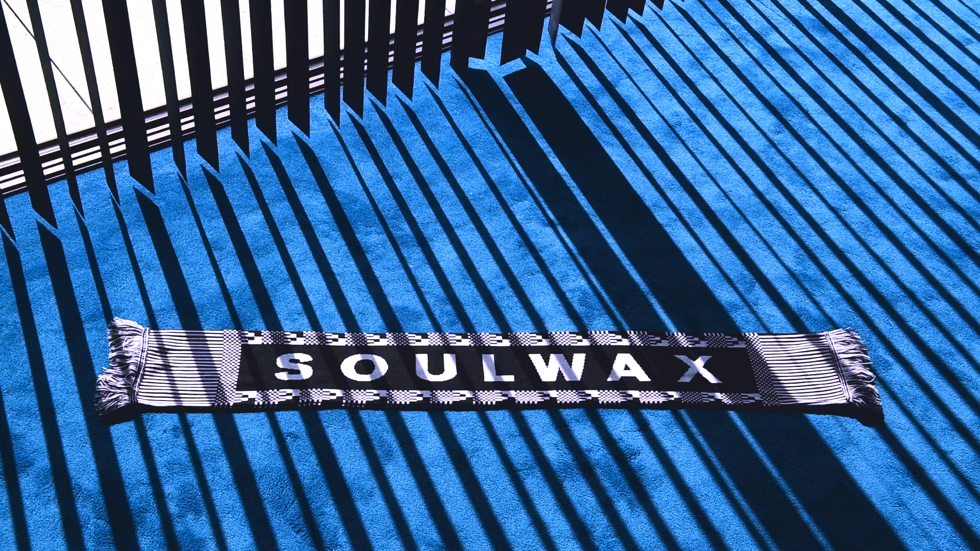 A scarf with "Soulwax" written on it lays on a blue carpet